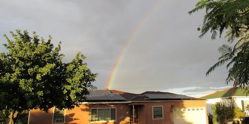 Home with rooftop solar panels under a rainbow